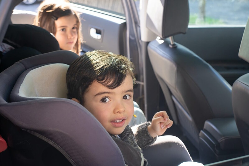 Two children in a car seat smiling at the camera.
